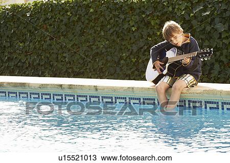 Stock Image - Boy playing guitar by pool. Fotosearch