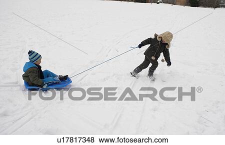 Stock Photo - Boy pulling his friend on a sledge. Fotosearch