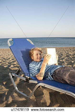 Boy reading on sunlounger View Large Photo Image Stock Photo - Boy reading on sunlounger. Fotosearch