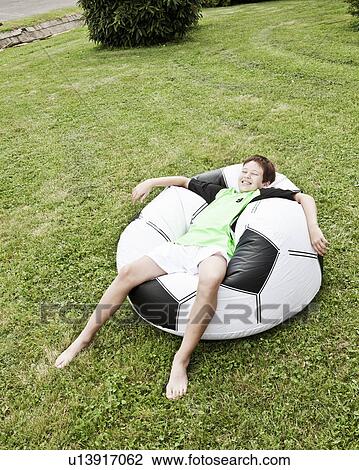 Boy relaxing on inflated giant football View Large Photo Image Stock Image - Boy relaxing on inflated giant football. Fotosearch