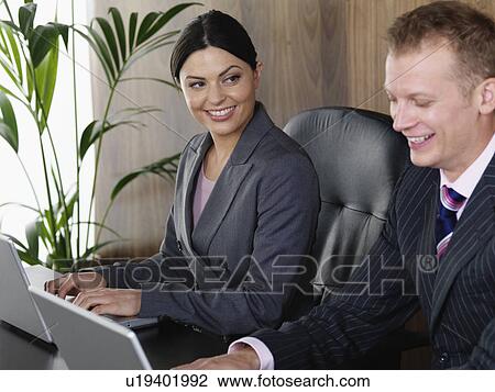 Stock Image - Business man and woman at desk. Fotosearch