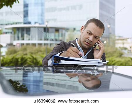 Stock Image - Businessman with paperwork on top of car. Fotosearch