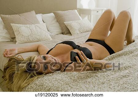 Stock Photography - Busty young woman on bed with cell phone. Fotosearch