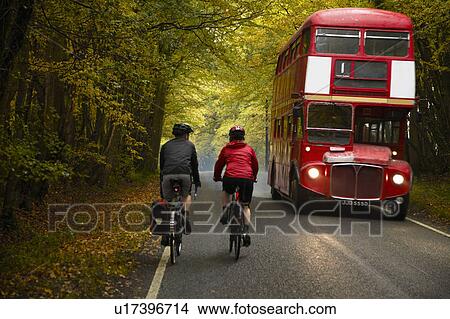 Picture - Couple cycling next to bus in country. Fotosearch