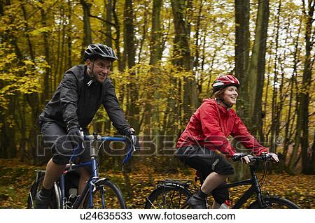 Couple cycling surrounded by trees View Large Photo Image Stock Image - Couple cycling surrounded by trees. Fotosearch