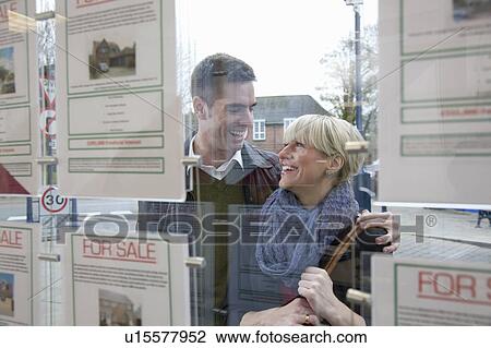 Stock Image - Couple looking into estate agents window. Fotosearch
