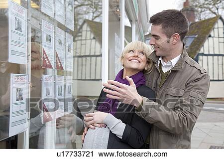Stock Image - Couple looking into estate agents window. Fotosearch