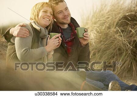 Couple on beach having coffee from flask View Large Photo Image Picture - Couple on beach having coffee from flask. Fotosearch