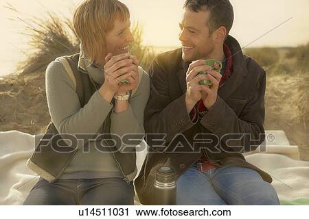 Couple on beach having coffee from flask View Large Photo Image Stock Image - Couple on beach having coffee from flask. Fotosearch