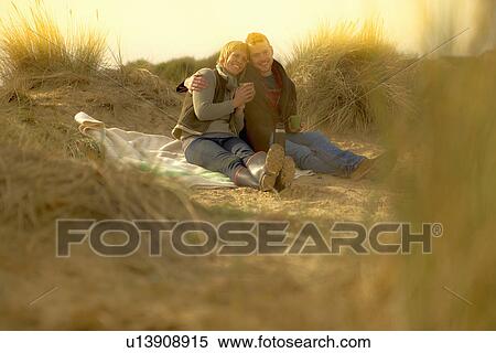 Stock Photography - Couple on beach having coffee from flask. Fotosearch