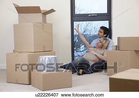 Stock Photo - Couple sat amongst boxes in apartment. Fotosearch