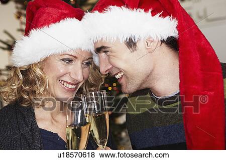 Couple with xmas caps clinking glasses View Large Photo Image Stock Photo - Couple with xmas caps clinking glasses. Fotosearch