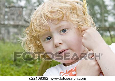 Stock Image - Curly haired boy on swing looking. Fotosearch