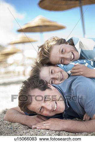 Dad with two sons in a pile on beach View Large Photo Image Stock Image - Dad with two sons in a pile on beach. Fotosearch