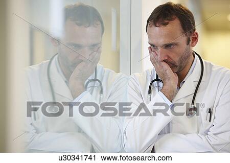 Stock Image - Doctor against a window, thinking. Fotosearch