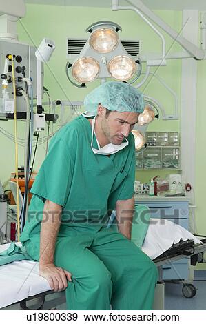 Stock Photo - Doctor with scrubs on couch, thoughtful. Fotosearch