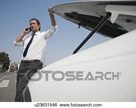 Stock Photograph - Driver on the phone with broken car. Fotosearch