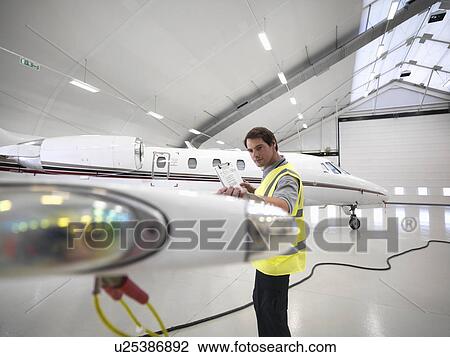 Stock Image - Engineer inspecting jet aircraft. Fotosearch