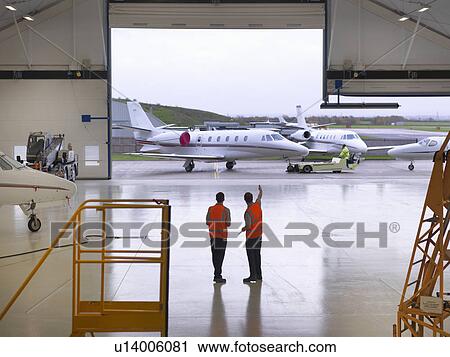Stock Image - Engineers in jet aircraft hangar. Fotosearch