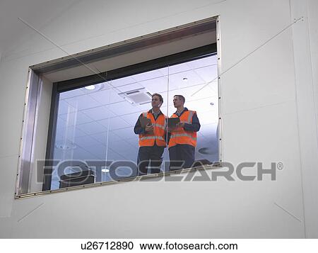 Stock Image - Engineers look out of window into hangar. Fotosearch