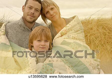 Stock Photo - Family cuddling under quilt on beach. Fotosearch