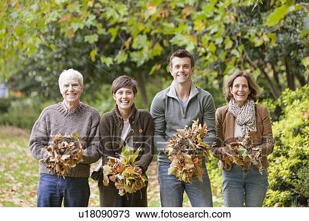 Stock Image - Family holding a bunch of leaves in park. Fotosearch