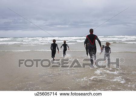 Picture - Family running in to the sea in wetsuits. Fotosearch