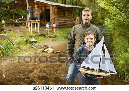 Stock Image - Father and son holding sailing boat. Fotosearch