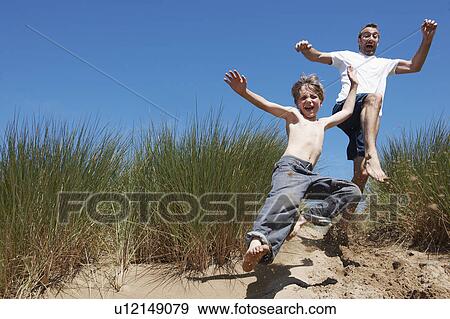 Stock Photo - Father and Son jumping in sand dunes. Fotosearch