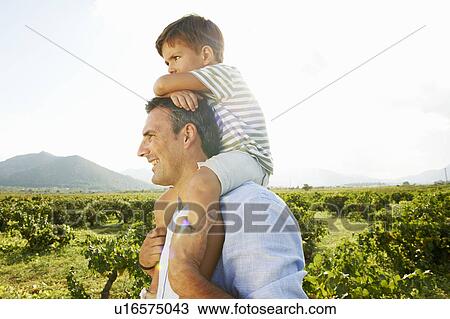 Stock Image - Father and son piggy backing in vineyard. Fotosearch