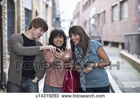 Stock Image - Friends sharing mobile in street. Fotosearch