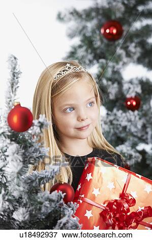 Stock Photo - Girl by a chritmas tree, with a present. Fotosearch