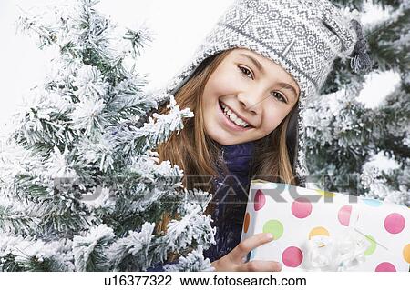 Girl holding a gift, beside snowy trees View Large Photo Image Stock Image - Girl holding a gift, beside snowy trees. Fotosearch
