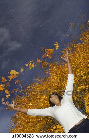 Stock Image - Girl in autumn throwing leaves up. Fotosearch