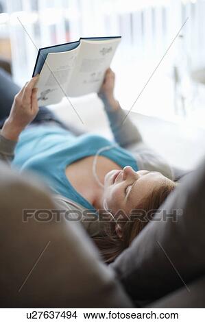 Picture - Girl lying on sofa reading a book. Fotosearch