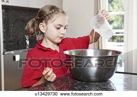 Stock Image - Girl pouring water in to mixing bowl. Fotosearch