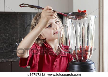 Stock Image - Girl putting fruit in blender. Fotosearch
