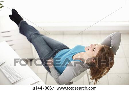 Stock Photo - Girl reclining on chair next to desk. Fotosearch