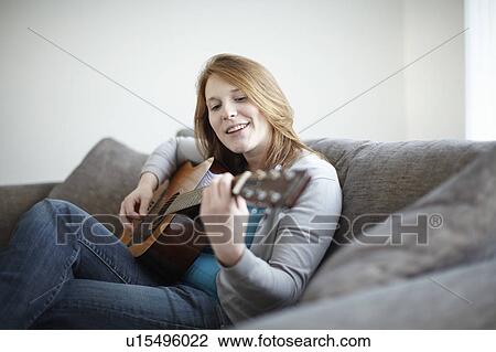 Girl sitting on sofa playing guitar View Large Photo Image Stock Image - Girl sitting on sofa playing guitar. Fotosearch