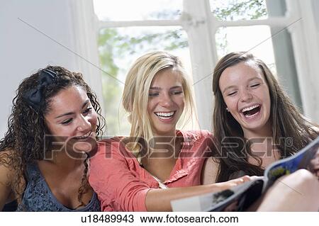 Stock Image - Girlfriends laugh looking at magazine. Fotosearch