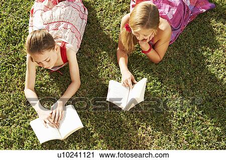 Girls lying on grass reading books View Large Photo Image Stock Image - Girls lying on grass reading books. Fotosearch