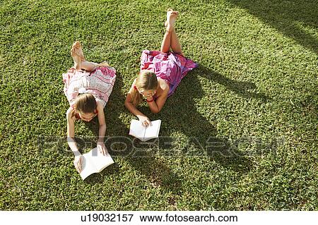 Stock Photo - Girls lying on grass reading books. Fotosearch