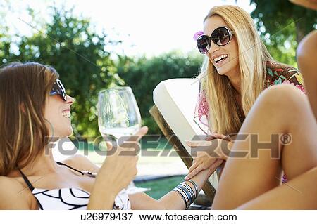 Stock Photo - Girls relaxing by the pool on sun beds. Fotosearch