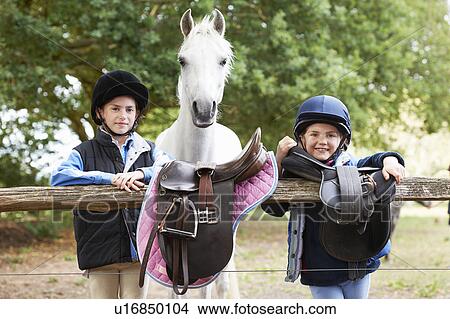 Picture - Girls with pony holding saddles. Fotosearch