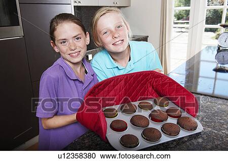 Stock Image - Girls with tray of fresh cooked cakes. Fotosearch