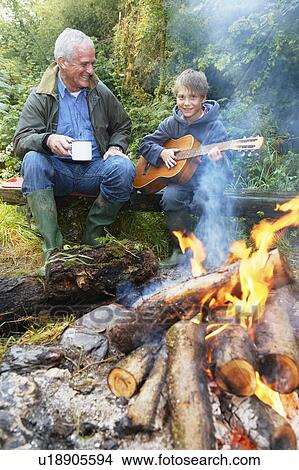 Picture - Grandfather and grandson by campfire. Fotosearch