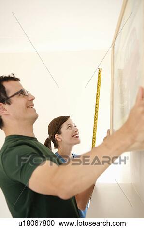 Stock Image - Happy couple hang a picture. Fotosearch