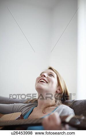 Happy girl playing guitar on sofa View Large Photo Image Stock Photo - Happy girl playing guitar on sofa. Fotosearch
