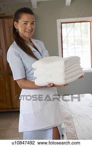 Stock Image - Hotel maid in room with pile of towels. Fotosearch