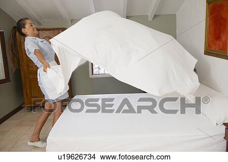 Picture - Hotel maid putting throwing sheet on bed. Fotosearch